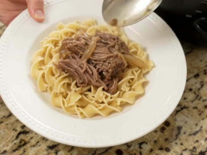 Slow cooker French onion garlic butter roast with caramelized onions and gravy, served on a white plate