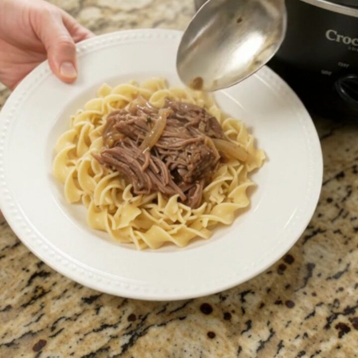 Slow cooker French onion garlic butter roast with caramelized onions and gravy, served on a white plate