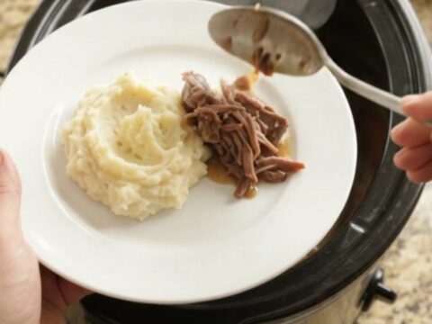 Fork-tender beef roast with shallots and carrots in a slow cooker, glistening with butter sauce.