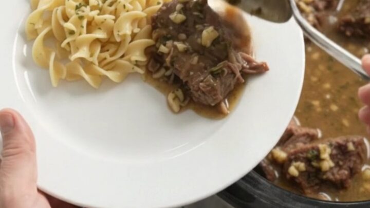 Slow-cooker beef roast with mushrooms and gravy in a black crockpot