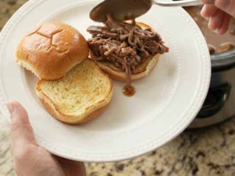 Fork-tender pot roast with portobello mushrooms in glossy brown gravy, served in a black slow cooker.
