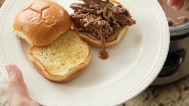 Fork-tender pot roast with portobello mushrooms in glossy brown gravy, served in a black slow cooker.