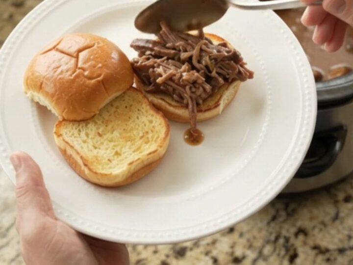 Fork-tender pot roast with portobello mushrooms in glossy brown gravy, served in a black slow cooker.