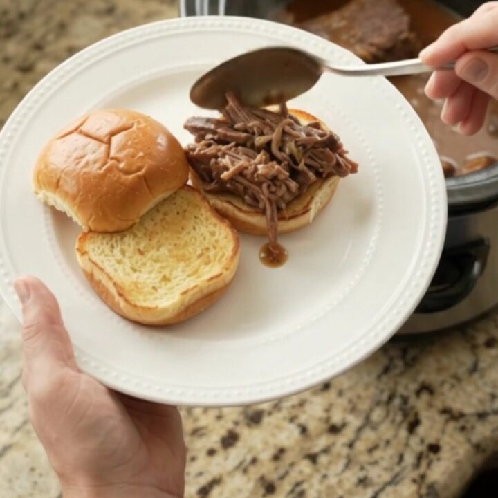 Fork-tender pot roast with portobello mushrooms in glossy brown gravy, served in a black slow cooker.