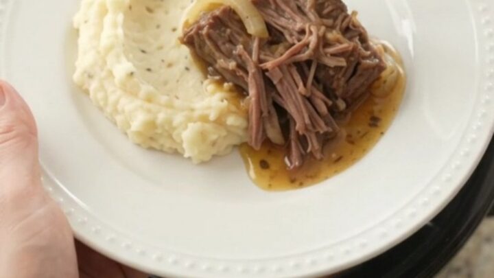 Slow-cooker bottom round roast with peppers, onions, and butter in a black ceramic crock.