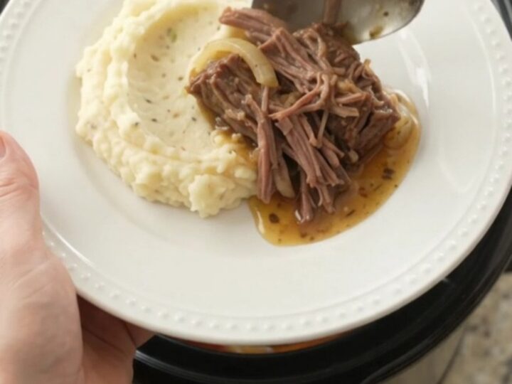 Slow-cooker bottom round roast with peppers, onions, and butter in a black ceramic crock.