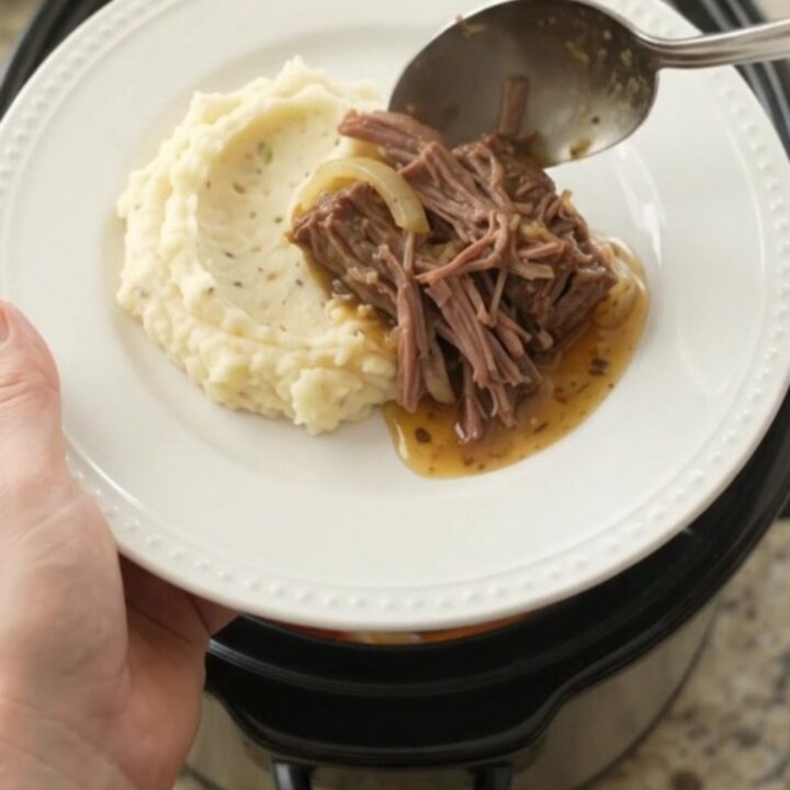 Slow-cooker bottom round roast with peppers, onions, and butter in a black ceramic crock.