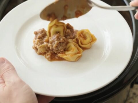 Slow cooker filled with cheesy tortellini and sausage, topped with melted Italian cheese and Parmesan crust
