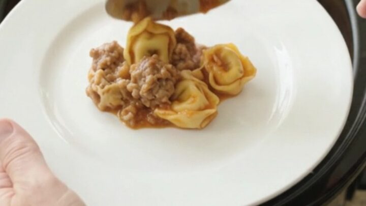 Slow cooker filled with cheesy tortellini and sausage, topped with melted Italian cheese and Parmesan crust
