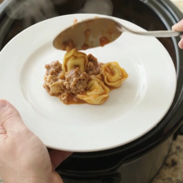 Slow cooker filled with cheesy tortellini and sausage, topped with melted Italian cheese and Parmesan crust