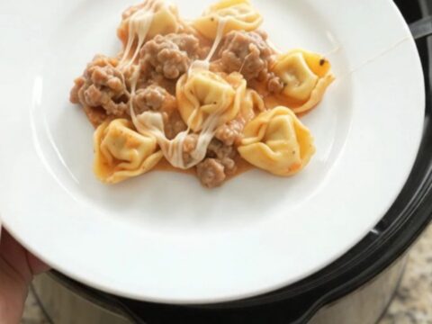 Slow cooker tortellini with sausage, marinara, and melted mozzarella, served in a bowl.