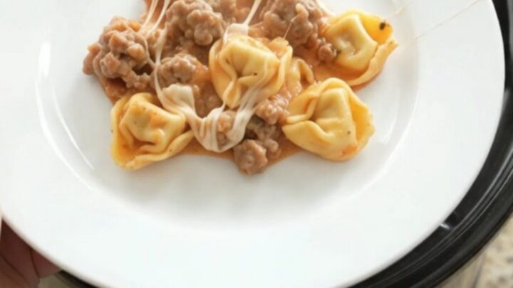 Slow cooker tortellini with sausage, marinara, and melted mozzarella, served in a bowl.