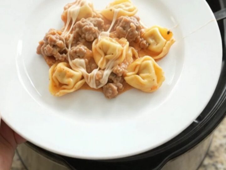 Slow cooker tortellini with sausage, marinara, and melted mozzarella, served in a bowl.