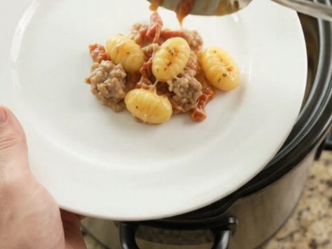 Crockpot Parmesan Sausage Tuscan Gnocchi in a black slow cooker, topped with melted cheese and steam rising.