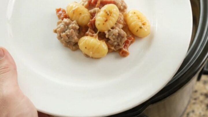Crockpot Parmesan Sausage Tuscan Gnocchi in a black slow cooker, topped with melted cheese and steam rising.