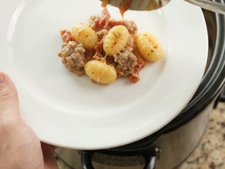 Crockpot Parmesan Sausage Tuscan Gnocchi in a black slow cooker, topped with melted cheese and steam rising.
