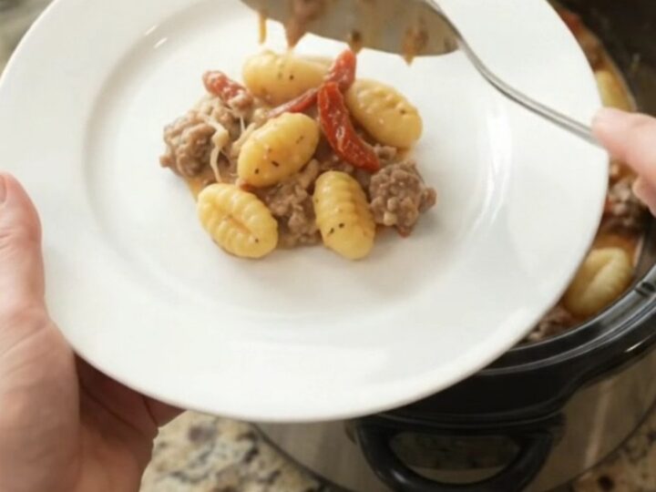 A slow cooker filled with creamy sausage gnocchi, topped with melted provolone and sun-dried tomatoes.