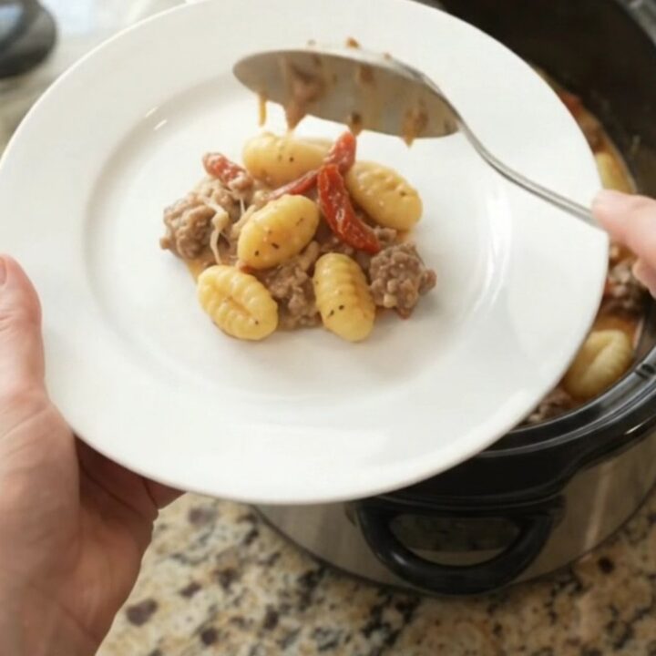 A slow cooker filled with creamy sausage gnocchi, topped with melted provolone and sun-dried tomatoes.