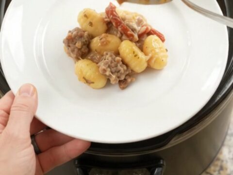 Creamy slow cooker gnocchi with sausage and melted cheese in a black crockpot