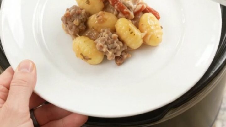 Creamy slow cooker gnocchi with sausage and melted cheese in a black crockpot