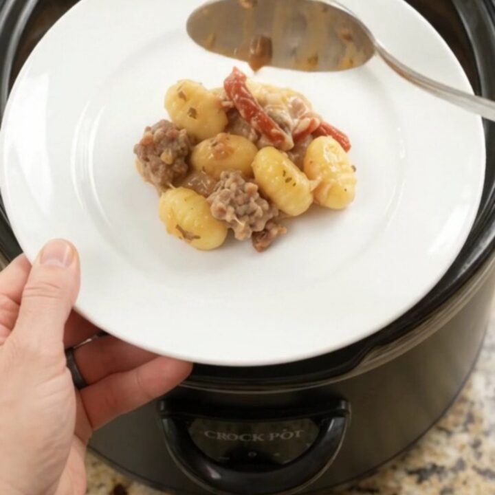 Creamy slow cooker gnocchi with sausage and melted cheese in a black crockpot