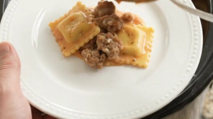Slow cooker filled with creamy sausage vodka ravioli topped with melted provolone and ricotta dollops