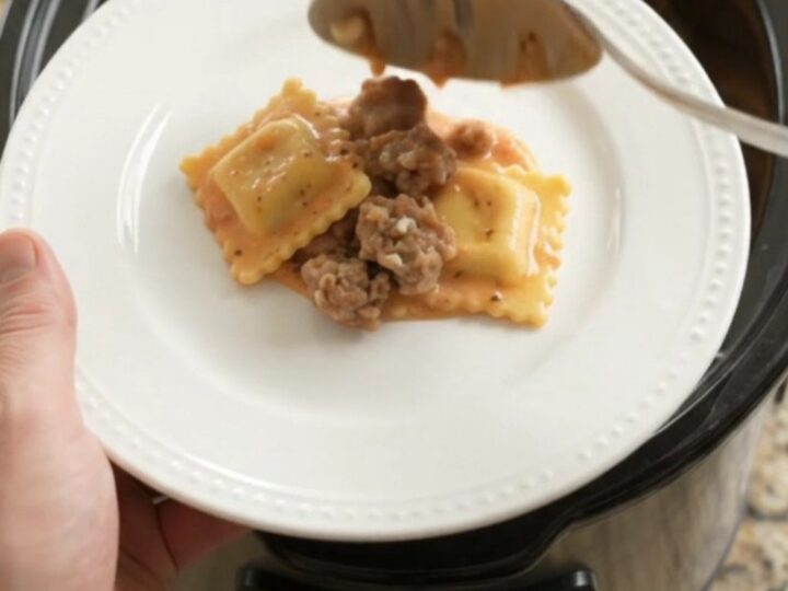 Slow cooker filled with creamy sausage vodka ravioli topped with melted provolone and ricotta dollops