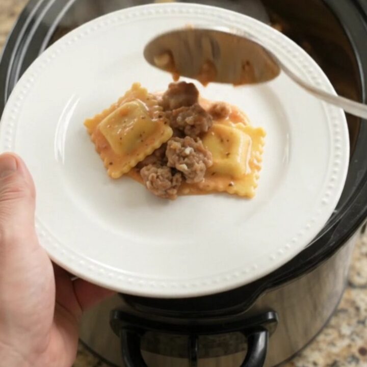 Slow cooker filled with creamy sausage vodka ravioli topped with melted provolone and ricotta dollops