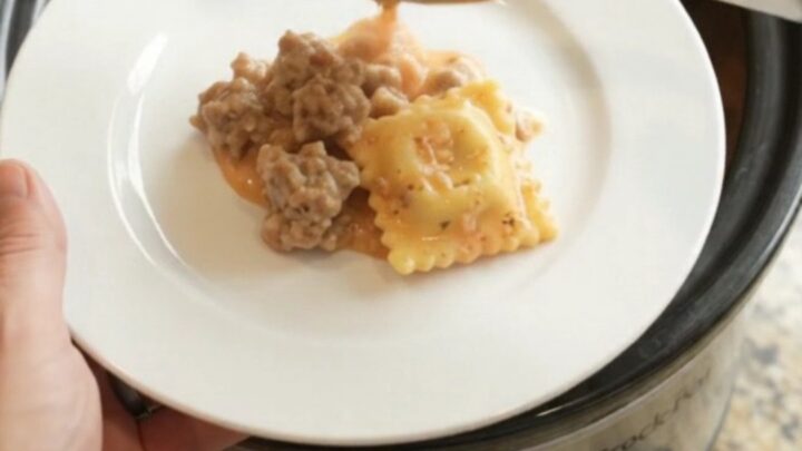 Slow cooker filled with bubbling sausage vodka ravioli topped with melted Italian cheeses