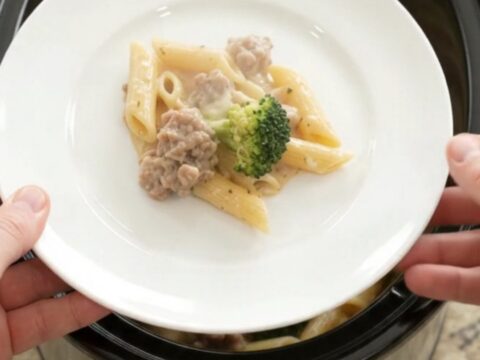 Slow cooker filled with creamy sausage Alfredo penne and broccoli, topped with melted mozzarella