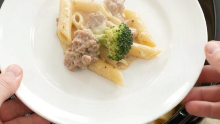 Slow cooker filled with creamy sausage Alfredo penne and broccoli, topped with melted mozzarella