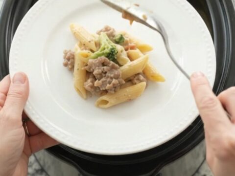 Slow cooker filled with creamy sausage Alfredo penne, topped with melted provolone and ricotta dollops