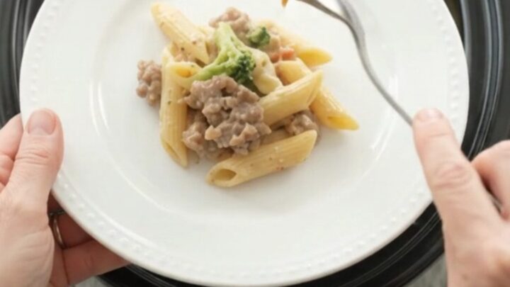 Slow cooker filled with creamy sausage Alfredo penne, topped with melted provolone and ricotta dollops
