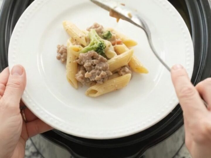Slow cooker filled with creamy sausage Alfredo penne, topped with melted provolone and ricotta dollops