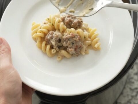 Slow cooker filled with creamy cavatappi pasta, sausage crumbles, and melted fontina cheese, topped with herbs.