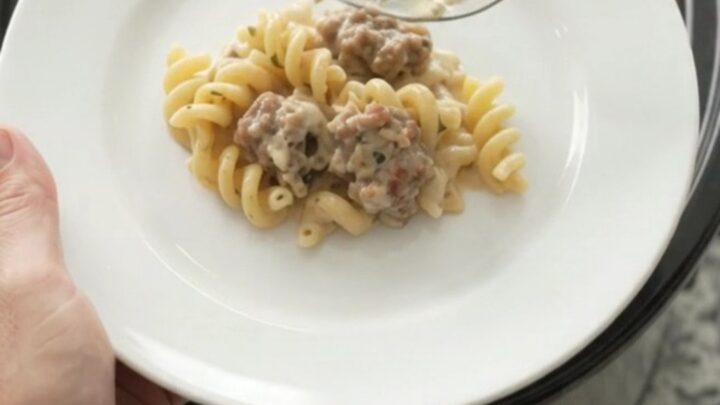 Slow cooker filled with creamy cavatappi pasta, sausage crumbles, and melted fontina cheese, topped with herbs.