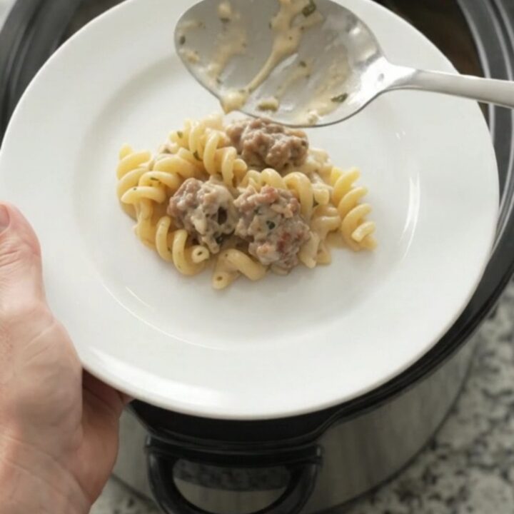 Slow cooker filled with creamy cavatappi pasta, sausage crumbles, and melted fontina cheese, topped with herbs.