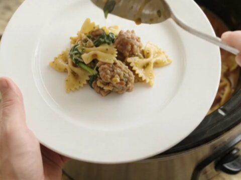 Slow cooker filled with creamy pesto farfalle, sausage, and melted mozzarella