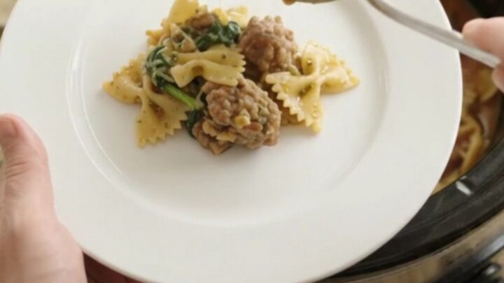Slow cooker filled with creamy pesto farfalle, sausage, and melted mozzarella