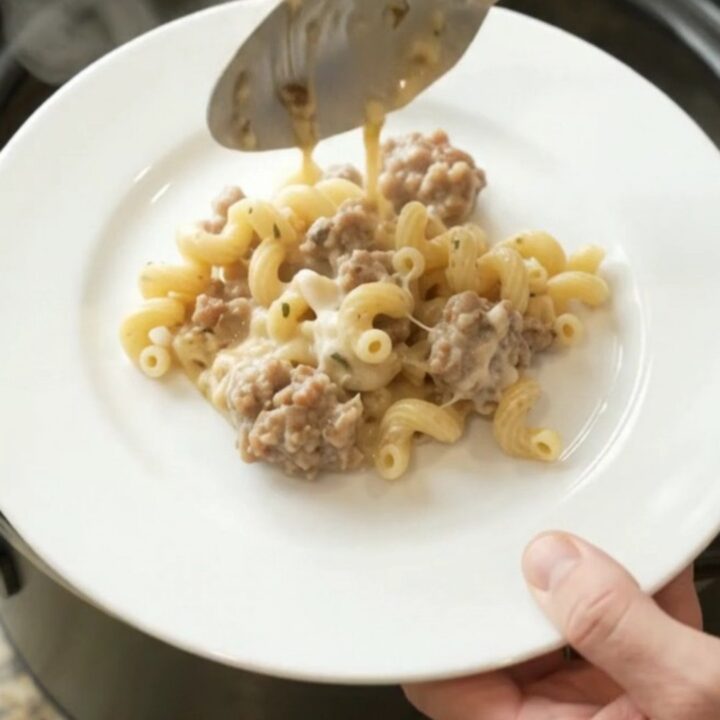 Creamy Crockpot sausage cavatappi with melted provolone and ricotta, served in a black slow cooker.