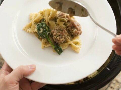 Slow cooker Parmesan sausage pesto farfalle in a black crockpot with melted cheese.