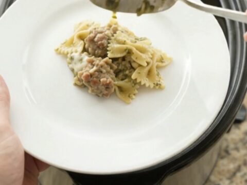 Slow cooker filled with creamy provolone sausage pesto farfalle, scooping a cheesy spoonful