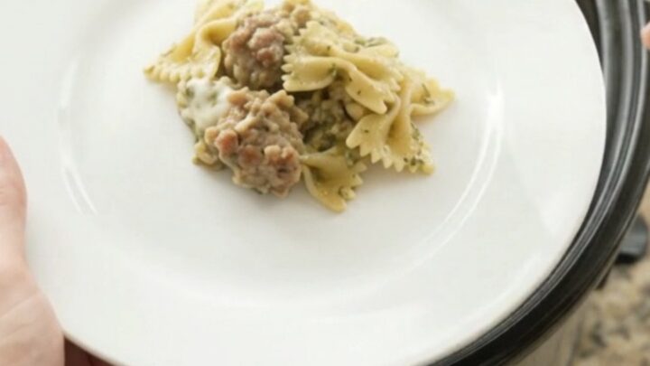 Slow cooker filled with creamy provolone sausage pesto farfalle, scooping a cheesy spoonful