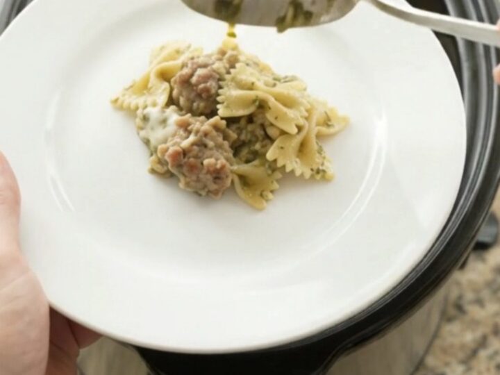 Slow cooker filled with creamy provolone sausage pesto farfalle, scooping a cheesy spoonful