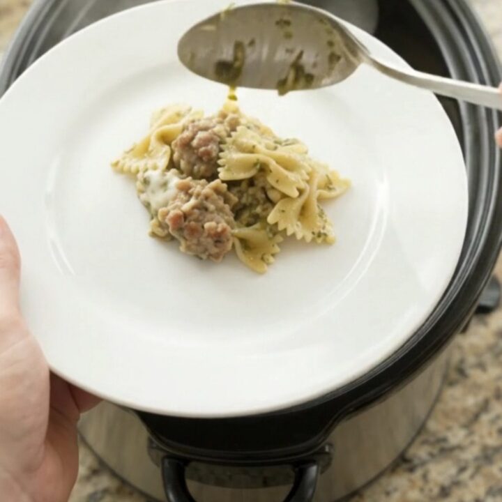 Slow cooker filled with creamy provolone sausage pesto farfalle, scooping a cheesy spoonful