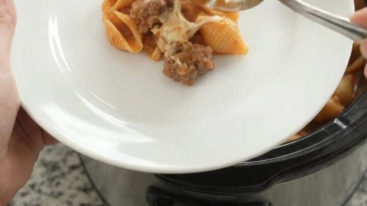 Slow cooker filled with creamy sausage and red pepper pasta topped with melted mozzarella