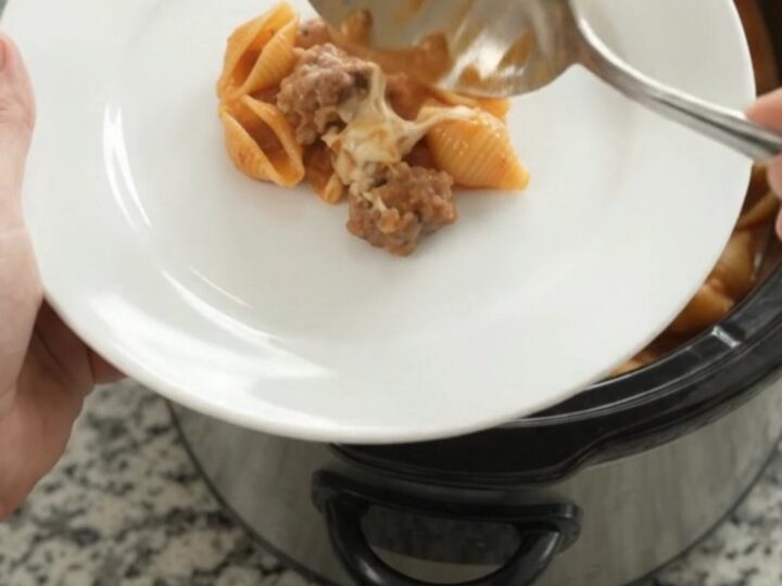Slow cooker filled with creamy sausage and red pepper pasta topped with melted mozzarella