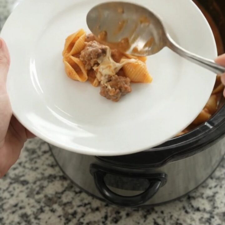 Slow cooker filled with creamy sausage and red pepper pasta topped with melted mozzarella