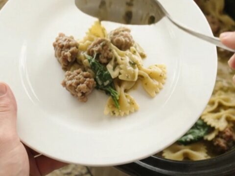 Creamy slow cooker pasta with Italian sausage, spinach, and melted cheese in a black crockpot