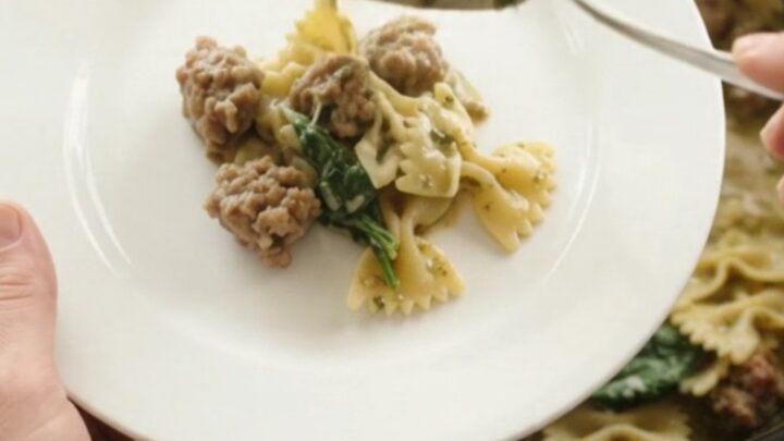 Creamy slow cooker pasta with Italian sausage, spinach, and melted cheese in a black crockpot